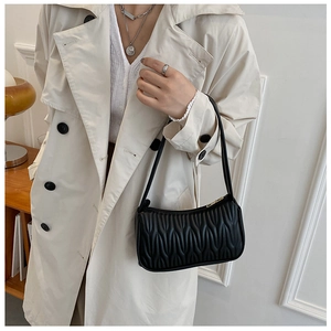 Detail of black underarm bag featuring wave pleats and gold zipper on beige trench coat