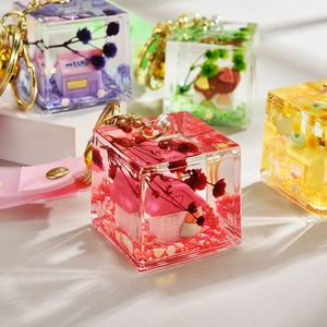 Detail of red acrylic cube keychain with miniature house and dried flowers inside