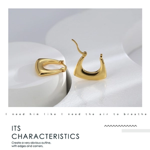 Detail view of golden geometric U-shaped earrings on a minimalist white stone background