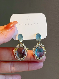 Detailed close-up of vintage gold earrings with blue cat eye stone and zircon accents