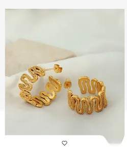 Detailed view of wave-shaped gold earrings with beaded texture on white fabric