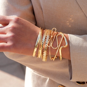 Close-up of a 6-piece gold geometric twisted cuff bracelet set worn over a beige suit