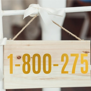 Detail of wooden hanging plaque with numbers and silk bow on white metal stand