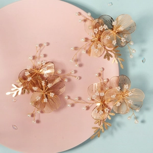 Detail of three handmade gold wire flower hair clips with white beads on a pink plate