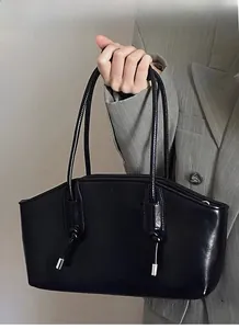 Detail of glossy black trapezoid tote with knotted long handles on grey blazer