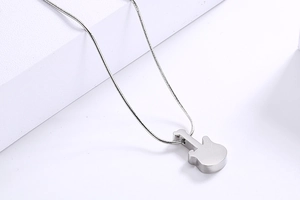 Close-up of a silver guitar pendant on a sleek snake chain over a white block
