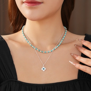 Detail of a layered necklace with turquoise beads and a clover pendant on a model
