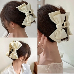 Detail of cream satin bow hair claw clip on model's updo from multiple angles