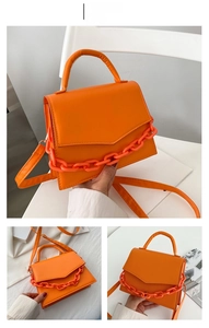 Detail view of orange leather small square handbag with decorative chunky chain and strap