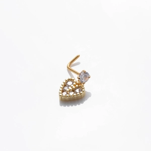 Detailed view of heart-shaped gold nose stud with a clear zircon inlay on a white background