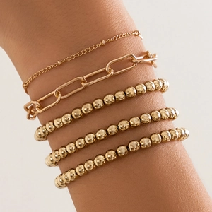 Close-up of layered gold beaded and paperclip link bracelets worn on a model's wrist