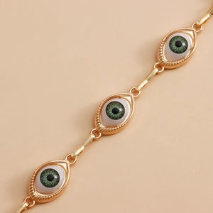 Macro shot of gold-plated evil eye link chain with green iris and white enamel detail