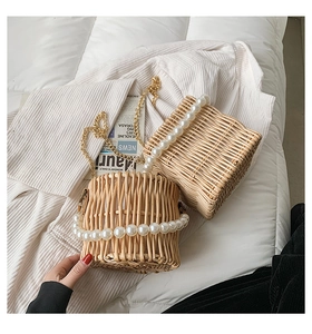 Detail of hand-woven straw bucket bag featuring elegant pearl handle and gold chain strap