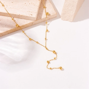 Minimalist gold tassel chain necklace with beads on stone background display