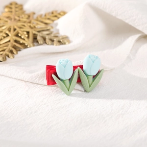 Detail of red hair clip with blue tulips and green leaves on white fabric background