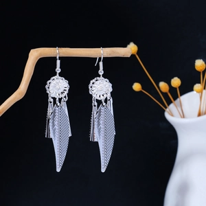Macro detail of silver feather earrings hanging on a branch with flower vase accent