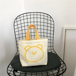 Detail of canvas bento bag with cute yellow bear face and handle on a grid chair