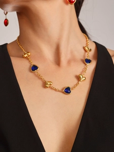 Detalle de collar de acero dorado 18K con corazones azules y pendientes rojos a juego