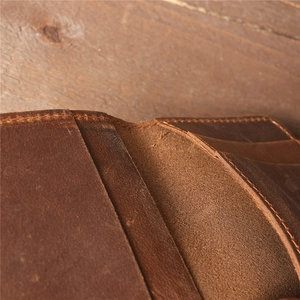 Vintage brown crazy horse leather card holder with hand-stitched detailing on wood surface