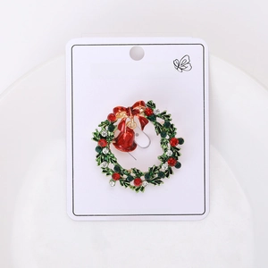 Detailed view of enamel Christmas wreath brooch with red bow and bells on paper card