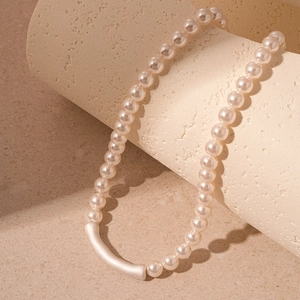 Vintage pearl necklace with a matte silver curved tube on a beige textured background
