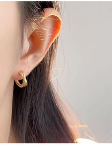 Close-up of a model wearing a golden twisted hoop earring with polished metal texture