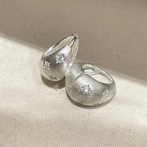 Macro shot of silver earrings with matte texture and embedded star detail for women