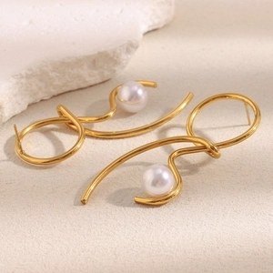 Detailed shot of gold-plated knotted line earrings with pearls on a textured stone base