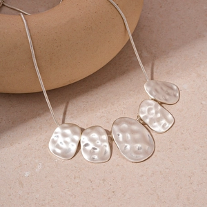 Macro shot of silver-toned hammered oval pendants on a fine snake chain necklace