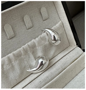 Macro shot of polished silver teardrop stud earrings on a beige textured jewelry display