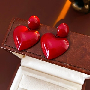 Close-up of red heart earrings on a brown leather jewelry box showing smooth texture