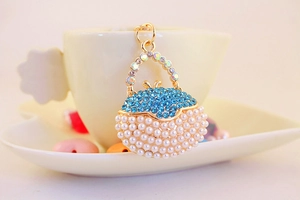 Close-up of golden handbag keychain featuring blue rhinestones and white pearls details