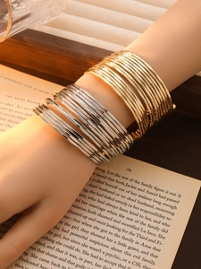 Detail of layered gold and silver wavy open cuffs on model against a vintage book