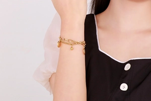 Detail of layered gold stainless steel bracelet with smiley face and ball charms on wrist