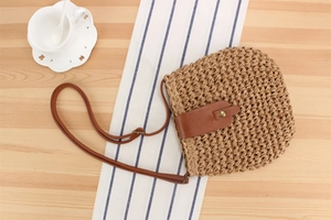 Close-up of paper rope woven bag with brown leather strap and gold buckle detail
