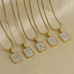 Close-up of 18K gold stainless steel snake chain necklaces with shell initial pendants