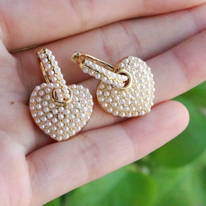 Detailed macro shot of heart-shaped gold earrings with white pearl inlay and U-clip design