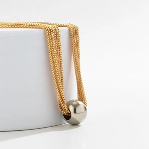 Detail of a minimalist gold box chain featuring a large polished metal ball pendant charm