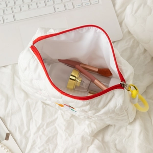 Macro view of white quilted dog makeup bag featuring red zipper and yellow ring puller