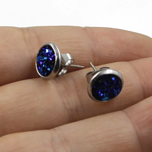 Detail shot of 8mm blue glitter stainless steel studs held on a finger for scale