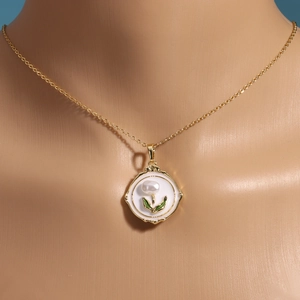 Elegant gold necklace with white enamel floral pendant and natural pearl on mannequin