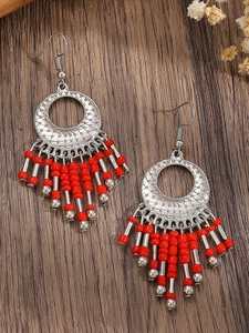 Detail of bohemian drop earrings with silver hollow patterns and red beaded tassels