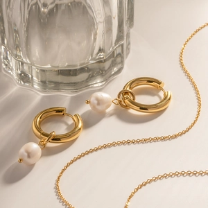 Artistic display of gold pearl hoop earrings and fine necklace on a soft surface
