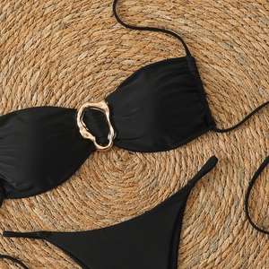 Detail of black bikini top with gold metal ring and textured swimsuit fabric on straw mat