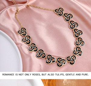Macro detail of vintage gold necklace with black enamel triquetra knots on pink satin
