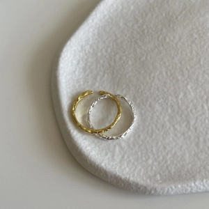 Detail of gold and silver wavy rings with hand-hammered texture on white ceramic plate