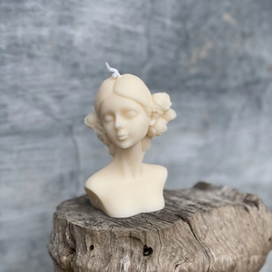 Artistic blindfolded girl bust candle with flowers on wood base against grey wall