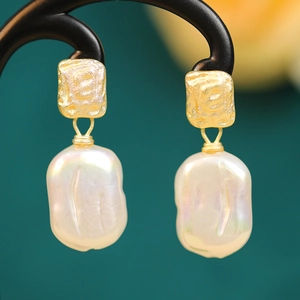 Macro detail of gold square studs with iridescent baroque pearl drop earrings