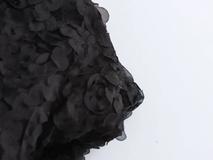 Nahaufnahme von schwarzem Textilgewebe mit strukturierten 3D-Blütenblättern und Spitzenmuster