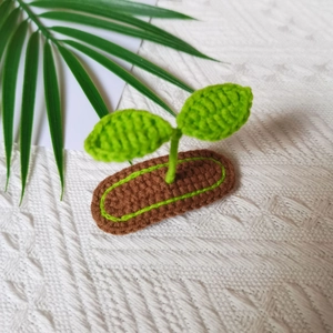 Detail of handmade crochet green sprout hair clip with dark brown base on soft fabric